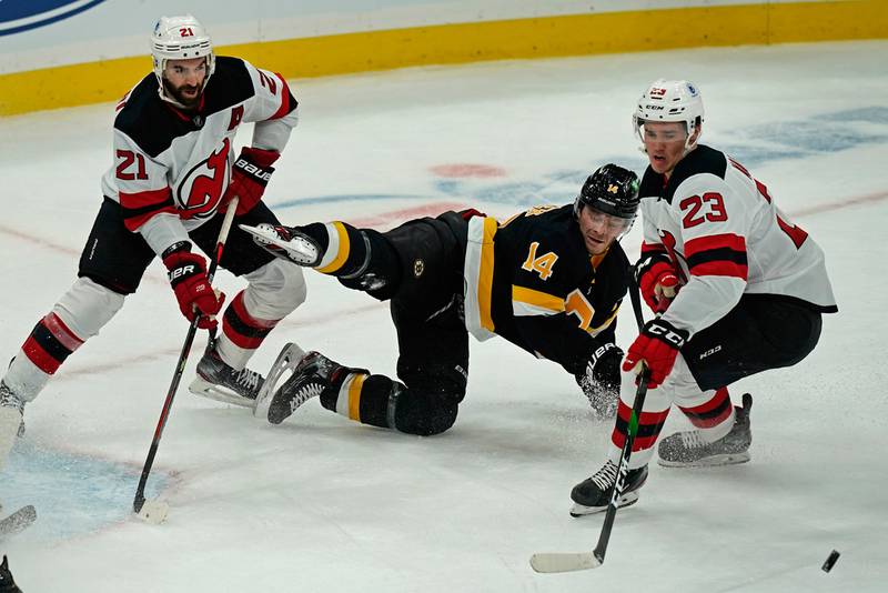 Boston Bruins right wing Chris Wagner (14) goes down on the ice as he competes for the puck against New Jersey Devils right wing Kyle Palmieri (21) and left wing Mikhail Maltsev (23) in the first period of an NHL hockey game, Thursday, Feb. 18, 2021, in Boston.