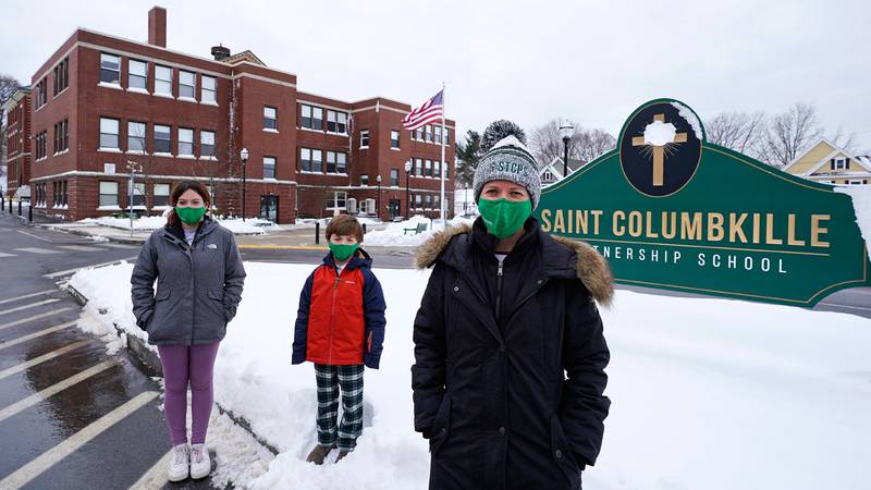 Head of School Jennifer Kowieski, right, poses with students Madeline Perry, of Brookline, left, and Landon Freytag, of Newton, center, outside the Saint Columbkille Partnership School, a Catholic school, Friday, Dec. 18, 2020, in the Brighton neighborhood of Boston. The families of both students decided to switch to the school, avoiding the challenges of remote learning at many public schools.