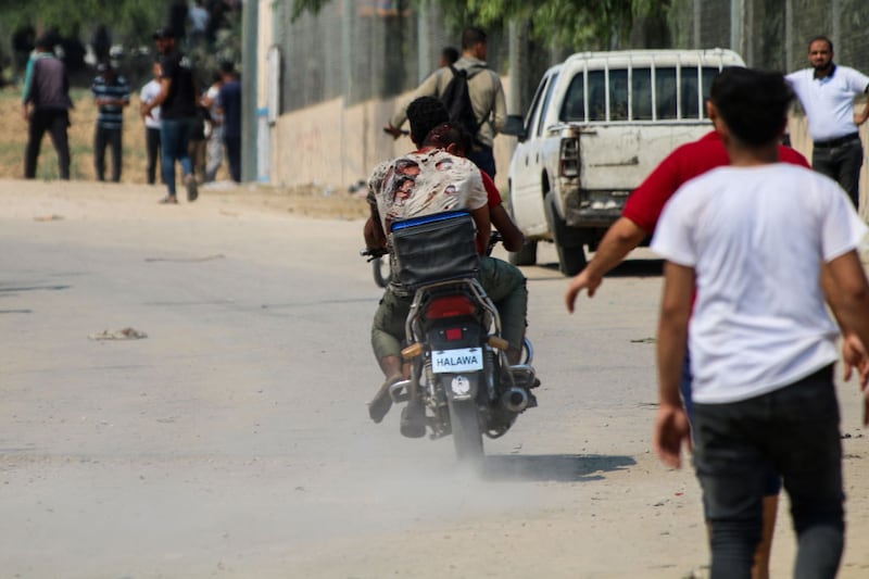 GAZA CITY GAZA - OCTOBER 7: A young man carries an injured man on his bicycle near the border fence between the Gaza Strip and Israel on October 7, 2023 in Gaza City, Gaza. The Palestinian militant group Hamas launched a missile attack on Israel today, with fighters simultaneously crossing the border from Gaza. Israel has declared a state of war. (Photo By Ahmad Hasaballah/Getty Images)